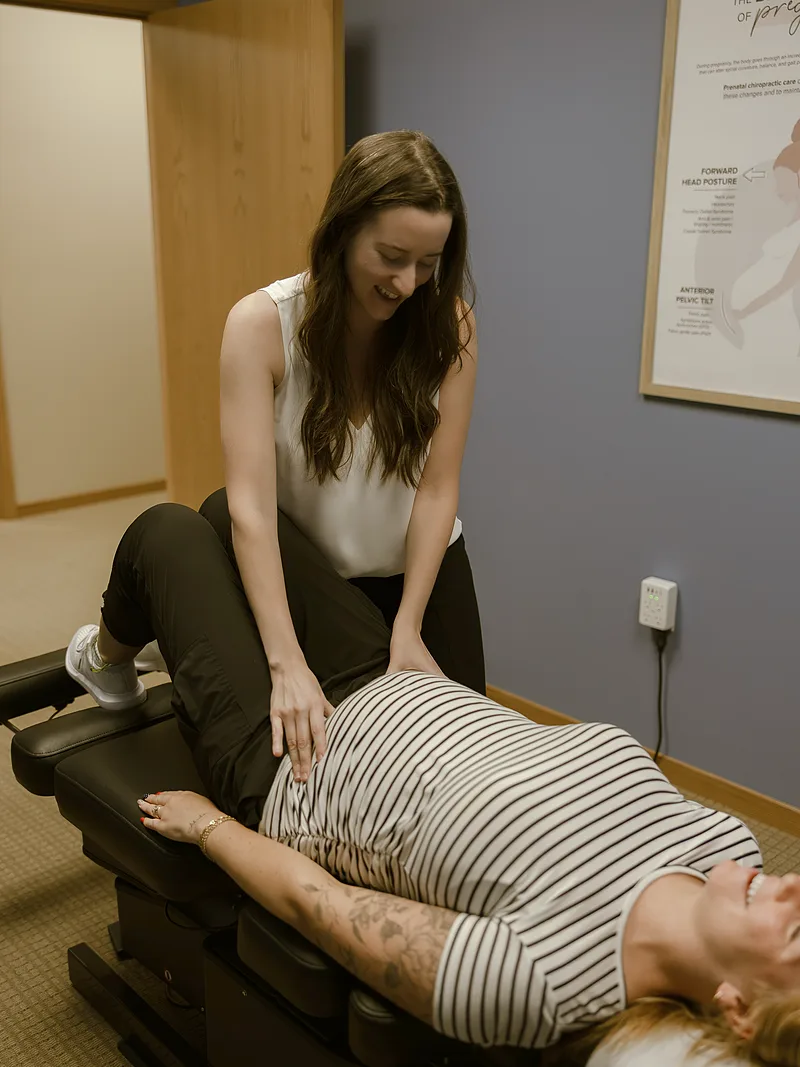 Dr. Moriah adjusting a patient beside a Biomechanics of Pregnancy poster